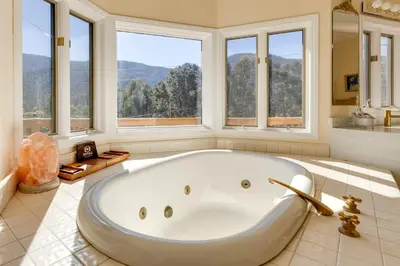a large white tub in a bathroom with windows at Game Room and Deck Modern Frazier Park Home! in Pine Mountain Club