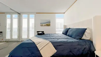 a bedroom with a bed with blue sheets and windows at Coastal Retreat Steps from the Santa Monica Beach in Los Angeles