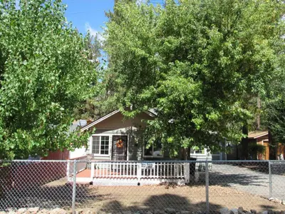 a house behind a fence with trees in front of it at Forest Moon Cottage in Big Bear City Airport