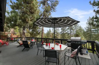 a deck with tables and chairs and an umbrella at Casita de Sergio - Peek-A-Boo Lake View, Walk to Lake, Fireplace in Big Bear Lake