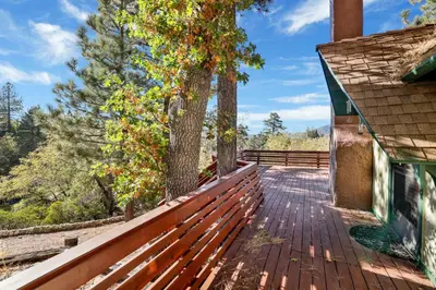 a wooden deck next to a house with a tree at Mountain Hideaway on Maryland by Big Bear Vacations in Big Bear Lake