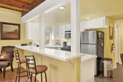 a kitchen with white cabinets and a refrigerator and chairs at Buttercup Snow Summit Condo by Big Bear Vacations in Big Bear Lake