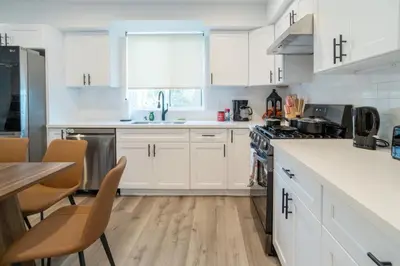 a white kitchen with white cabinets and a table at Stylish & Cozy Retreat Near USC & Downtown LA in Los Angeles