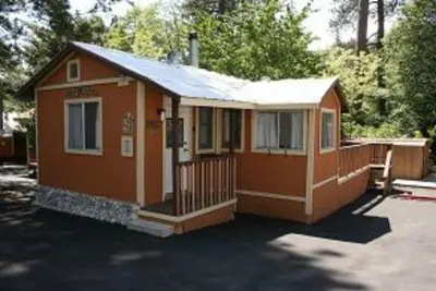 a small orange house with a porch and a driveway at Sleepy Hollow Cabins and Hotel in Crestline