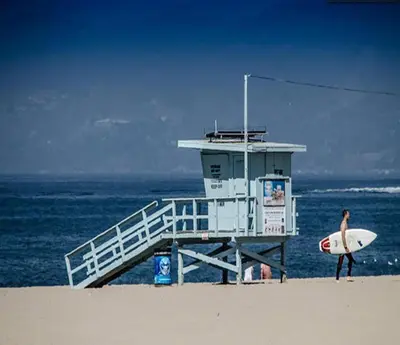 a person walking on the beach with a surfboard at Maison on the Beach in Los Angeles
