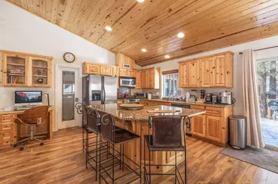 a kitchen with wooden cabinets and a island with bar stools at TimberWood Cabin- 3 Bdr - 2 Bth - Big Game room - Prime Location in Big Bear Lake in Big Bear Lake