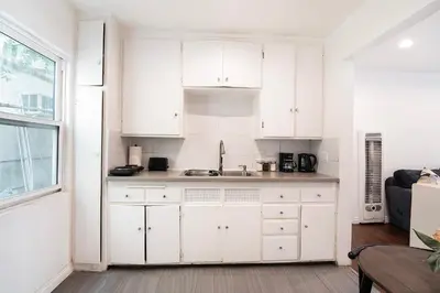 a white kitchen with white cabinets and a window at Ground-Floor 1-Bedroom by Beverly Hills Steps from Restaurants, Cafes and Shopping in Los Angeles