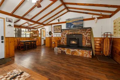 a living room with a stone fireplace and a table at Mountain Xscape - Hot Tub, Fireplace, Deck, Barbeque in Big Bear Lake