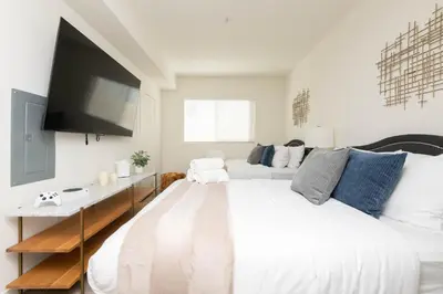 a white bedroom with a large bed and a tv at Hollywood Apartment Near Walk of Fame in Los Angeles