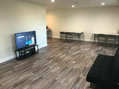 a room with a flat screen tv and tables and chairs at VWM Hostel in Los Angeles