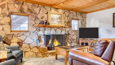 a living room with a stone wall with a fireplace at Lakefront w Private Dock Hot Tub Large Deck Views Lakeside on Lagunita in Big Bear Lake