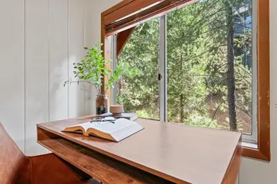 a table with a book on it next to a window at Cozy Owl Lodge, Central AC & Hea, Spa Tub & BBQ in Lake Arrowhead