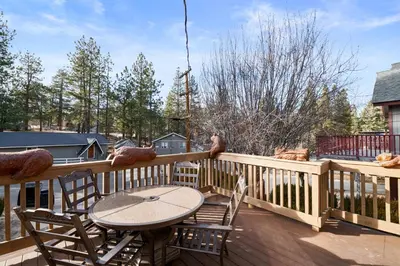 a table and chairs on a deck with a bird on the railing at Big Bear Cottage - Walk to Lake, Smart TV, Fireplace, Deck in Big Bear Lake