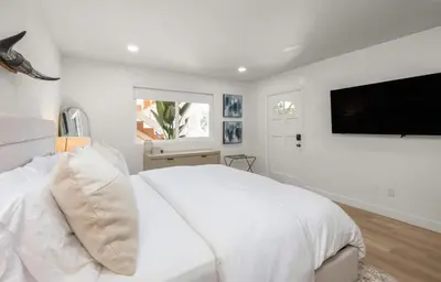 a white bedroom with a large bed and a flat screen tv at The South Bay Retreat in Redondo Beach