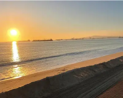 a beach with the sun setting over the water at Sea La Vie Beachhouse on the sand in Long Beach