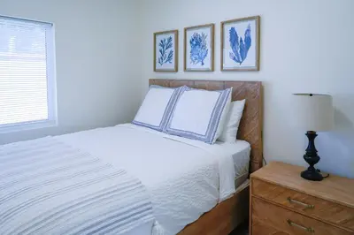 a bedroom with a white bed with a nightstand and pictures at Newly built vacation home with large backyard in Diamond Bar