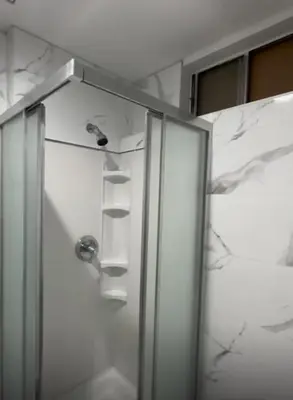 a shower stall with a glass door with shelves at Cozy 2 BR Apartment Glendale in Glendale