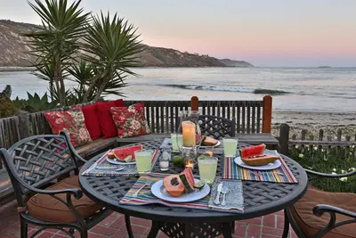 a table with plates of food and watermelon on the beach at Rincon Retreat by Paradise Retreats in Carpinteria