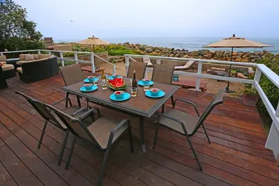 a wooden deck with a table and chairs and the ocean at Seacliff Beach House by Paradise Retreats in Ventura