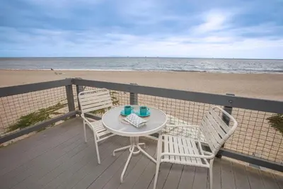 a table and two chairs on a deck near the beach at Seahorse Cottage by Paradise Retreats in Carpinteria
