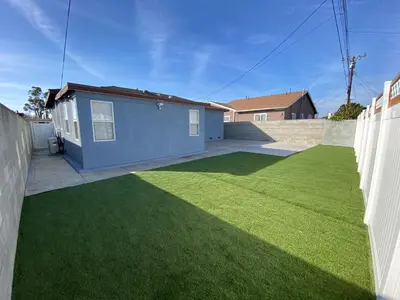 a yard with a blue house and green grass at HubCityJewel in Compton