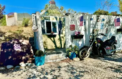a small house with a motorcycle parked next to a fence at Cozy Container in Devore Heights, California, for Glamping Getaways on Route 66 in Devore Heights