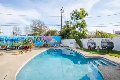 a swimming pool in front of a fence with a mural at Blue Haven Solar Pool Heat Parking Billiards in Long Beach