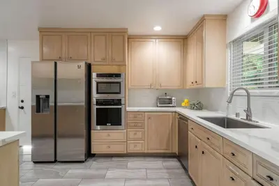 a kitchen with wooden cabinets and a stainless steel refrigerator at Overlooking Luxury - Pool Heat - Spa - Games in Pico Rivera