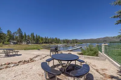 a table and two chairs and a picnic table and a lake at Big Bear Lakefront Lodge in Big Bear Lake