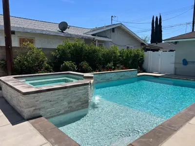 a swimming pool in a yard with a stone wall at Beautiful Remodel 3 Bedroom 2 bathroom Home with Pool & Jacuzzi in Fullerton