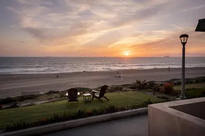 a sunset at the beach with two chairs and a table at New Listing The Nautilus Manhattan Beachfront Retreat in Manhattan Beach