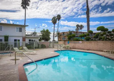 a swimming pool with chairs and a building and palm trees at Beautiful 1 Bed Beach Condo #224 in Carpinteria