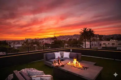 a living room with a fire pit on a balcony with a sunset at NEW Modern Oasis off Melrose - Rooftop - Pool in Los Angeles