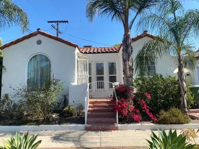 a white house with a palm tree and flowers at Spanish Cottage on Rosewood Avenue, Los Angeles , Melrose Village in Los Angeles