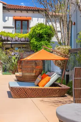 a wicker chair with an orange umbrella on a patio at Premier Suites at Marina-Venice with Luxe Pool, Gym & Hot Tub & More in Los Angeles