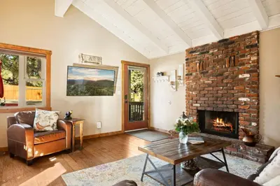 a living room with a brick fireplace and a table at Alpine Crest in Big Bear Lake in Big Bear Lake