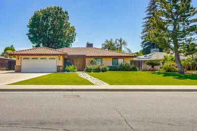 a house with a garage and a green yard at 7 Mi to Dtwn Poolside Paradise in Bakersfield! in Bakersfield