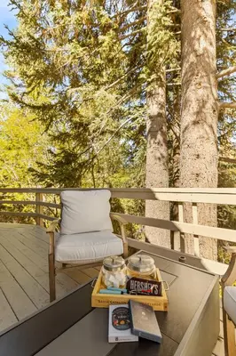 a table and a chair on a deck with trees at Chalet Vino - Snow Valley Mountain Resort in Green Valley Lake