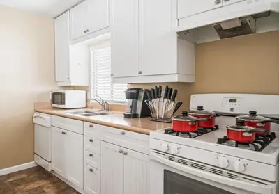 a kitchen with white cabinets and a stove with pots and pans at Serene Yard Porch at Signal Hill - Close to the Beach in Signal Hill