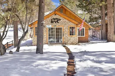 a log cabin in the snow with an american flag at Lily's Bear Cabin -Adorable Downtown Retreat Cottage in Big Bear Lake