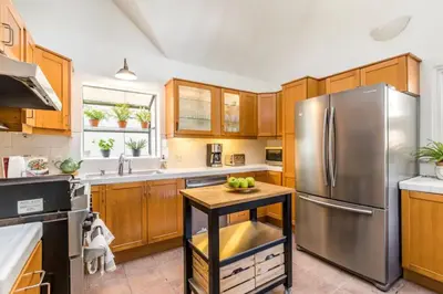 a kitchen with wooden cabinets and a stainless steel refrigerator at Chic Beach Bungalow 3 Blocks from the Sand in Manhattan Beach