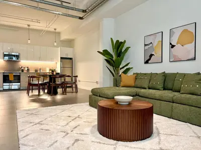 a living room with a green couch and a table at DTLA 2BR Loft with Hot Tub & Rooftop Pool! in Los Angeles