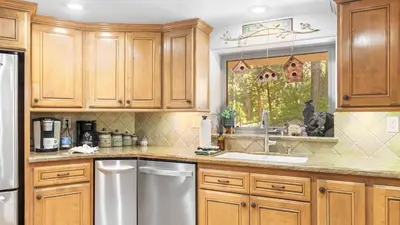 a kitchen with wooden cabinets and a dog looking out the window at The Fairway Hideaway by AvantStay Game Room Outdoor Dining Near Lake Arrowhead in Lake Arrowhead