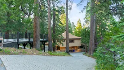 a house in the middle of a forest with a bridge at The Fairway Hideaway by AvantStay Game Room Outdoor Dining Near Lake Arrowhead in Lake Arrowhead