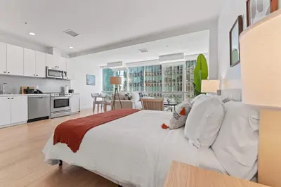 a white bedroom with a large bed and a kitchen at Stylist Downtown LA Gateway- Studio Apt in Los Angeles