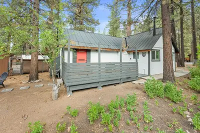 a white house with a red door in a yard at Cozy Knight Cabin - AC! Walk to Lake and Village in Big Bear Lake