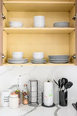a kitchen counter with plates and utensils on a shelf at Modern New 3B Home Fully Stocked & Cozy & Sunlight