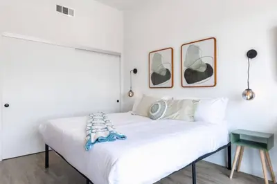 a white bed in a bedroom with two pictures on the wall at Chic Studio, Walk to Downtown With Skyline Views in Los Angeles