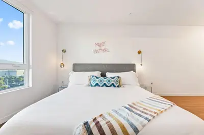 a white bedroom with a large bed and a window at Chic Studio with Stunning DTLA Views, Walk to Metro in Los Angeles