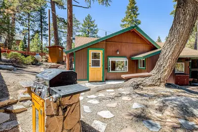 a house with a stove in front of a tree at Castle Rock Cabin #1 ~ Comfortable cabin with modern amenities and deck - near hiking and lake in Big Bear Lake